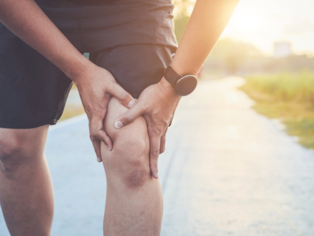 Injury from workout concept : Asian man use hands hold on his knee while running on road in the park. Shot in morning time, sunlight and warm effect with copy space for text or design