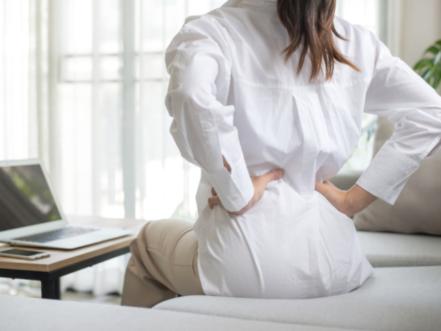 Working woman sitting on the sofa in the living room at home She used both hands to press down on the lower back. She is suffering from back pain from sitting for a long time.